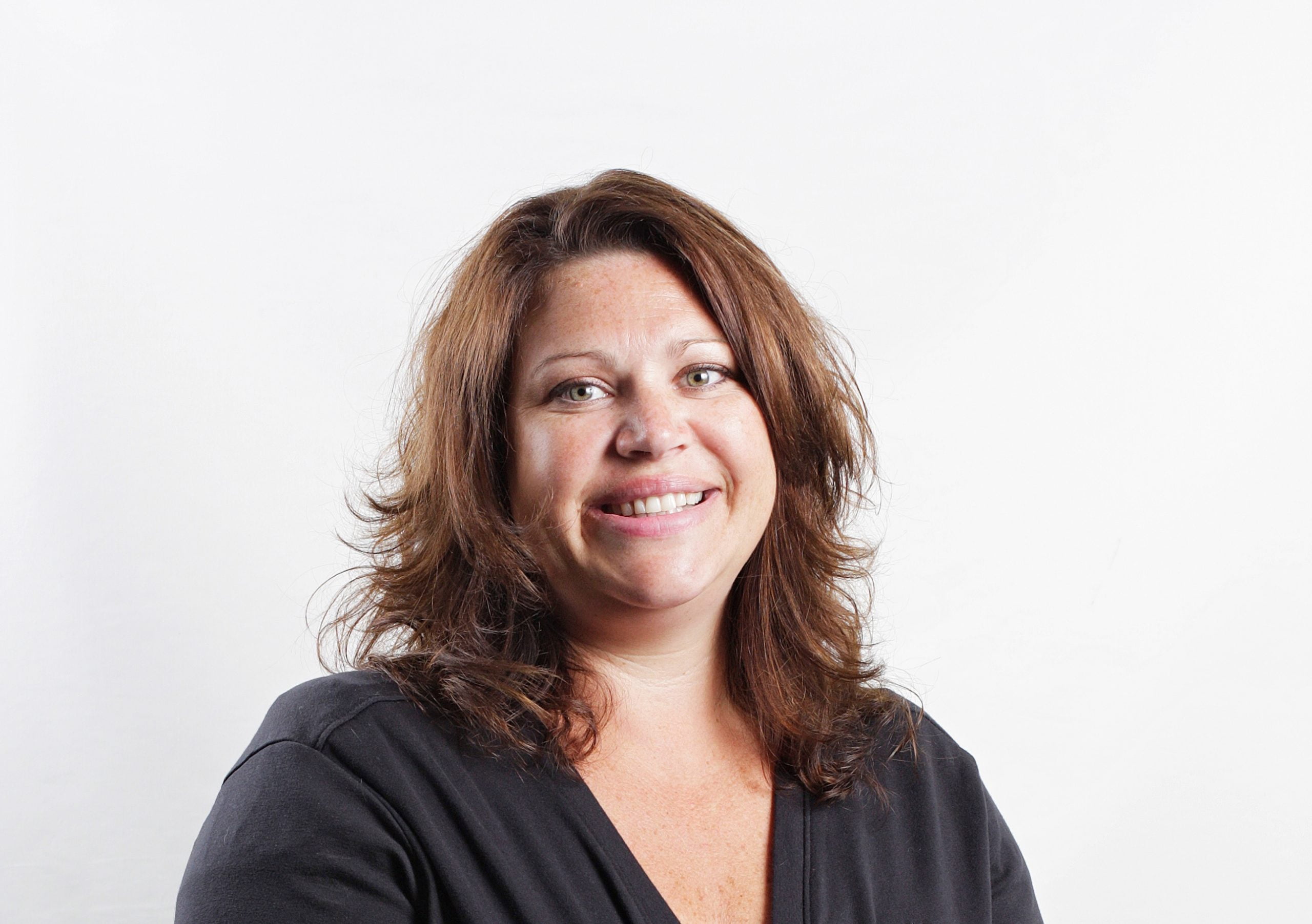 Portrait of Lori Bergland with shoulder‑length brown hair wearing a dark top, photographed against a plain light background.