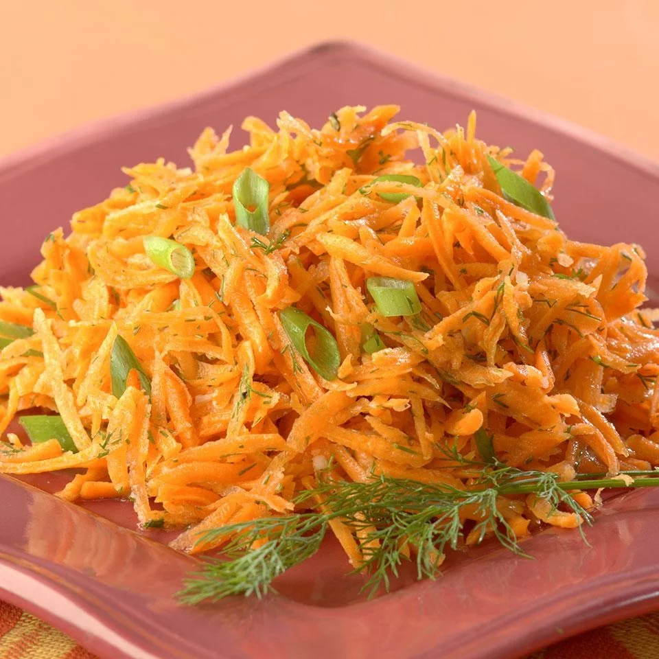 Plated lemony carrot salad–inspired dish with finely shredded carrots, fresh herbs, and green onion garnish served on a pink plate.