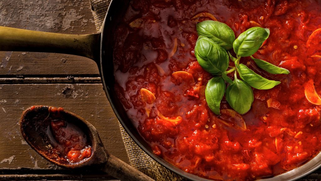 Classic marinara sauce in a sauce pan with some green garnish on a wooden table.