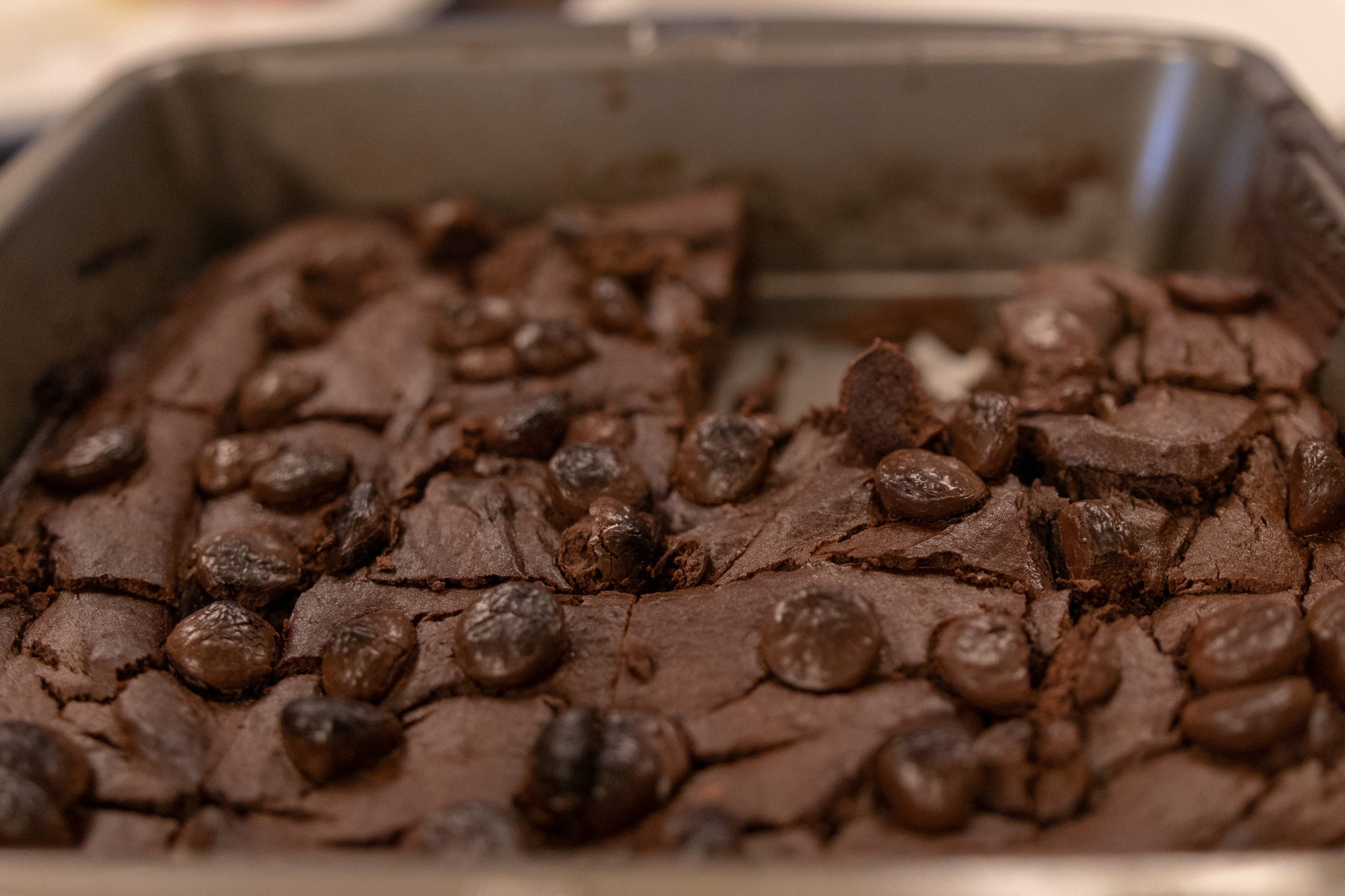 Pan of baked black bean avocado brownies cut into squares, topped with chocolate chips and shown from a close-up angle.