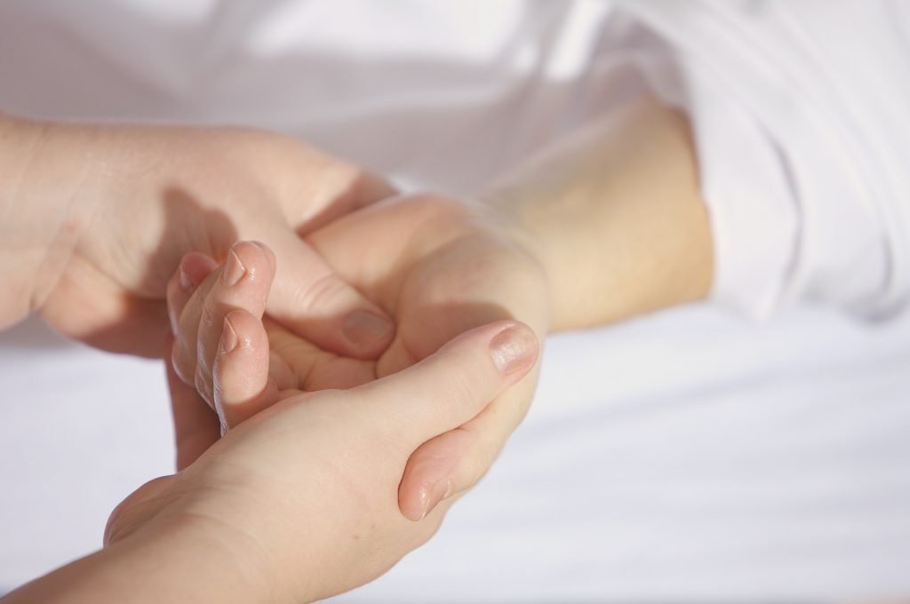 Close-up of two people’s hands, with one hand gently holding and supporting the other against a softly lit, neutral background.