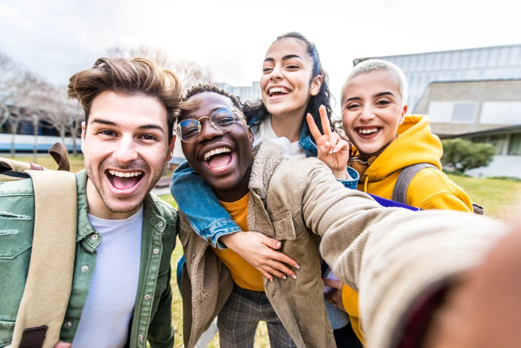Multiracial students company taking selfie portrait in university campus - Multi ethnic best friends laughing at camera outside - Teens having fun together - Youth culture and school concept