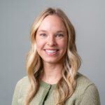 Portrait-style image showing psychologist Hanah Loders, a person with long wavy hair wearing a textured green sweater against a plain gray background.