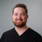 Dentist Casetin Lybbert wearing a dark V‑neck top is shown against a plain gray background.