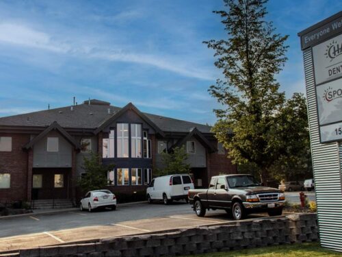 Exterior view of Urgent Care-Valley clinic building with a freestanding sign reading ‘Everyone Welcome’ and ‘CHAS Dental,’ showing the address ‘1502 N.’ Several parked vehicles, trees, and a landscaped stone wall are visible under a partly cloudy sky.
