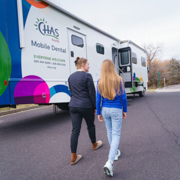 CHAS Health mobile dental clinic now open, parked outdoors as two people walk toward the clinic entrance.
