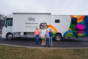 CHAS Health mobile dental clinic with mascot and three people standing in front.