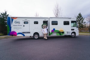 Chazzy standing beside a CHAS Health mobile dental clinic parked outdoors.