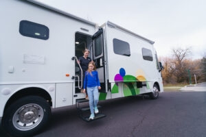Child walking down the steps of a mobile dental clinic with a staff member standing in the open doorway.