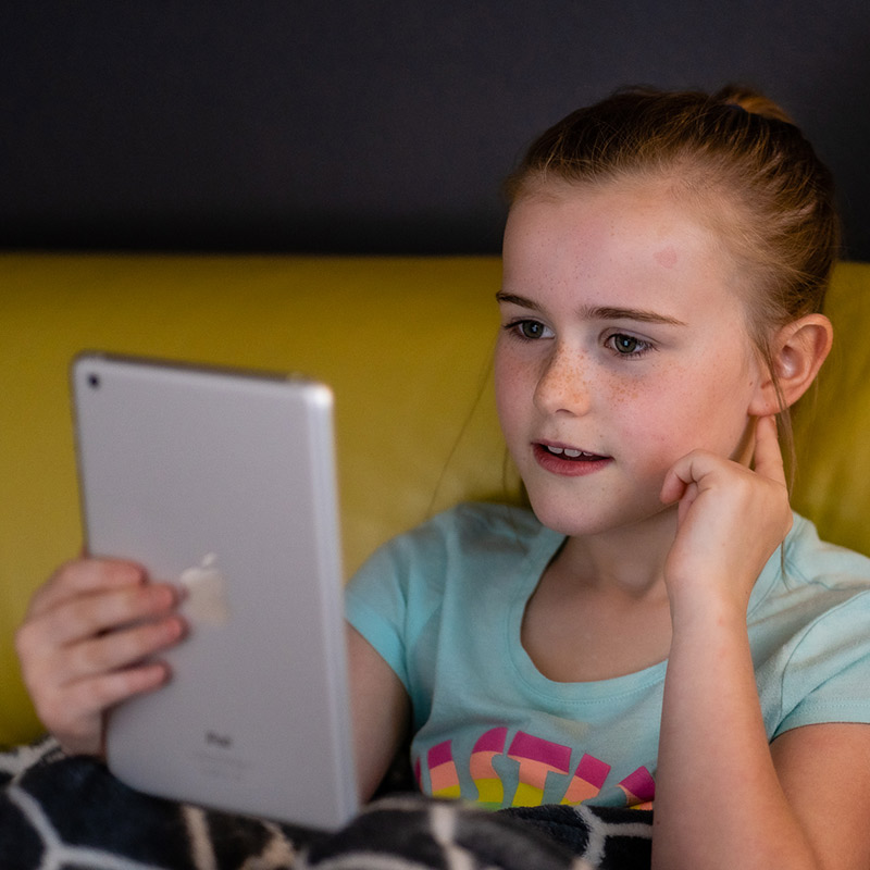 A child age 8–12 is using a silver iPad while sitting indoors.