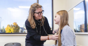 Healthcare provider using a stethoscope to examine a child during a clinic visit.