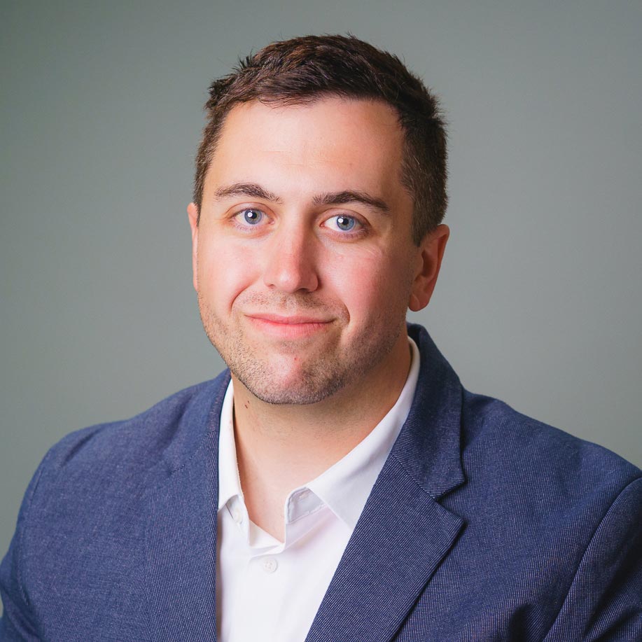 Professional headshot of a person wearing a blue blazer and white shirt against a gray background.