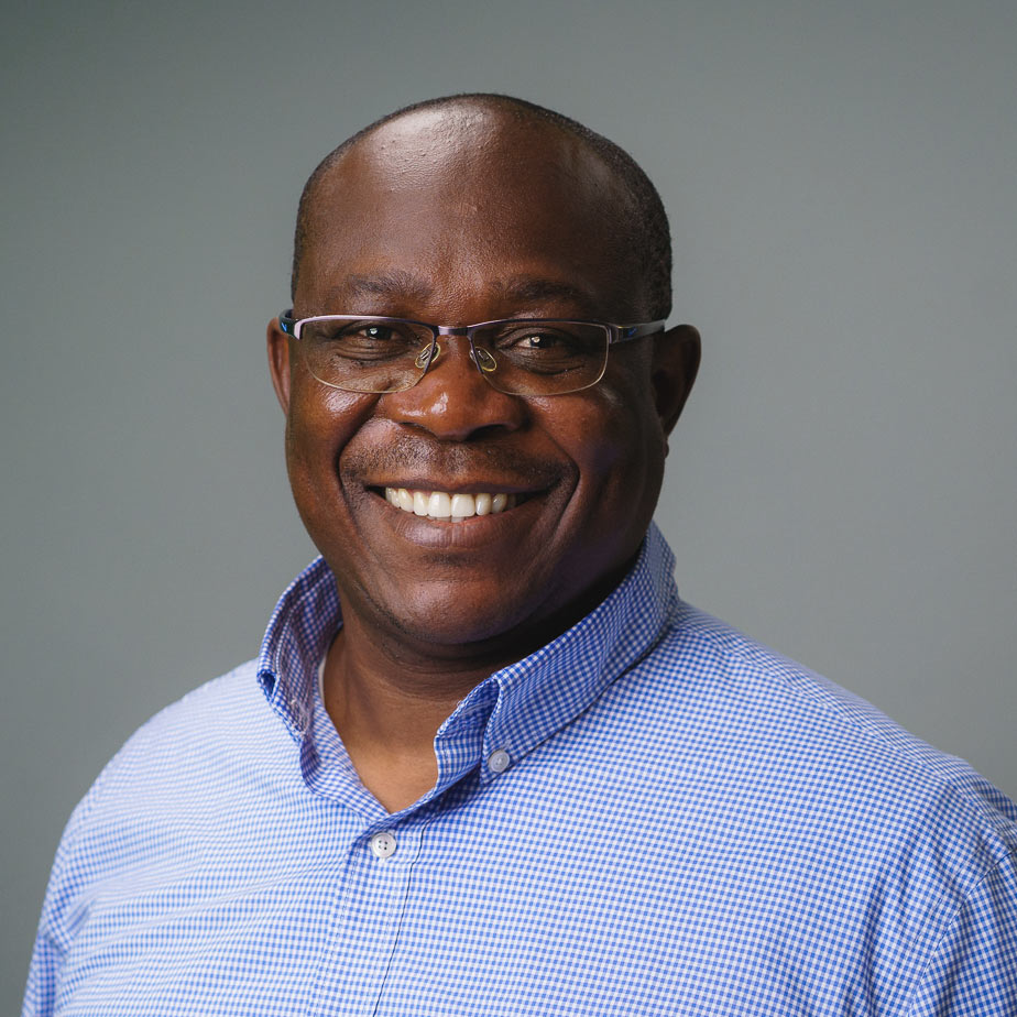 Professional headshot of a person wearing glasses and a light blue checkered button-down shirt, photographed against a plain gray background.
